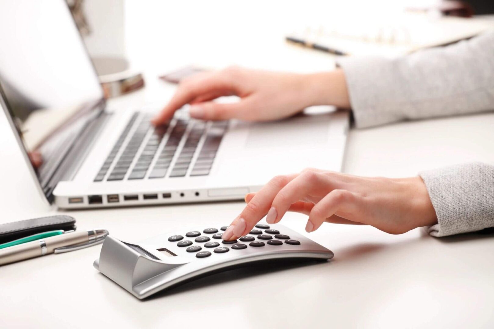 A person using a calculator on top of a laptop.